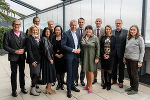 Bildbeschreibung: Eine Gruppe von Menschen steht für ein Porträtfoto zusammen. Im Hintergrund ist eine Glasfassade zu sehen.