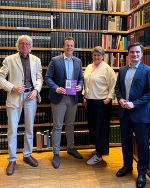 Eine Frau und drei Männer stehend vor einem Bücherregal