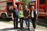 Drei Männer und eine Frau stehen vor Löschfahrzeugen der Feuerwehr.