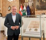 Ein Mann stehend, im gläsernen Kasten liegt ein historisches Dokument 
