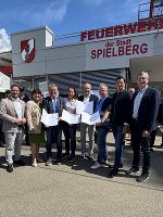 Gruppe von Menschen mit Urkunden vor einem Gebäude mit der Aufschrift 'Feuerwehr'.
