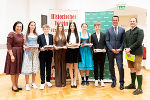 Gruppe von Menschen in festlicher Kleidung empfängt Auszeichnungen in einem Innenraum.