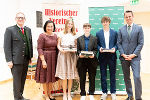 Gruppe von Menschen in festlicher Kleidung empfängt Auszeichnungen in einem Innenraum.