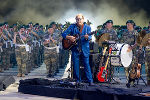 Bildbeschreibung: Mann spielt Gitarre vor einer Formation in Militäruniform.