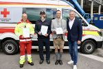 Vier Personen stehen nebeneinander vor einem Rettungsfahrzeug.