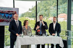 Vier Personen stehen nebeneinander. Im Hintergrund ist grüne Landschaft zu sehen.