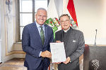 Bildbeschreibung: Ein Mann überreicht einem anderen Mann eine Urkunde.