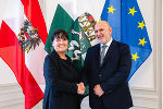 Zwei lächelnde Personen geben sich die Hand vor den Flaggen der Steiermark, Österreichs und der EU.