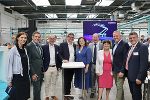 Gruppe von Menschen steht in einer modernen Industriehalle vor einem Bildschirm.