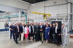 Gruppe von Menschen steht in einer modernen Industriehalle. Im Hintergrund sind Maschinen zu sehen.