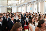 Gruppe junger Menschen in festlicher Kleidung bei einer Zeremonie in einem hellen Saal.