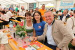 Festzelt mit freundlichen Menschen an einem Tisch. Im Hintergrund weitere Besucher und Dekoration.