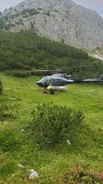Helikopter auf einer Wiese in Berglandschaft, im Hintergrund Felswände. Einsatzfahrzeug im Fokus.