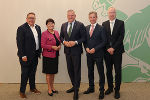 Fünf Personen in formeller Kleidung stehen nebeneinander und lächeln in die Kamera. Im Hintergrund eine grüne Wand.
