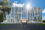 Bildbeschreibung: Ein mehrstöckiges Bürogebäude mit moderner Fassade, im Hintergrund die Sonne.