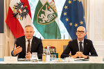 Zwei Personen in formeller Kleidung an einem Tisch vor den Flaggen von Österreich, Steiermark und der EU.